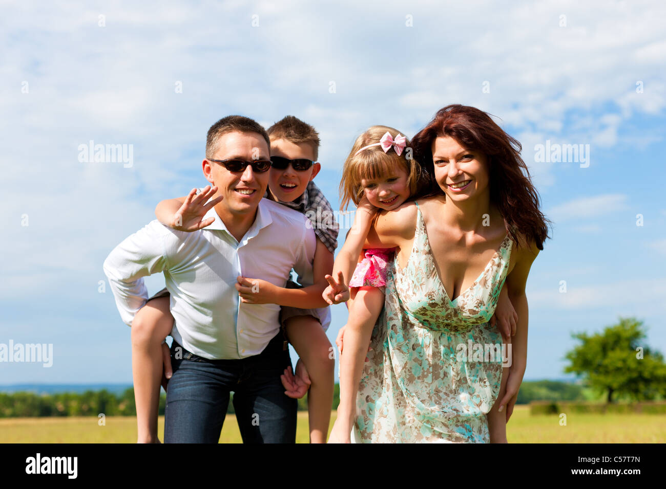 Glückliche Familie - Mutter, Vater, Kinder - stehend auf einer Wiese im Sommer Huckepack die Kinder Stockfoto