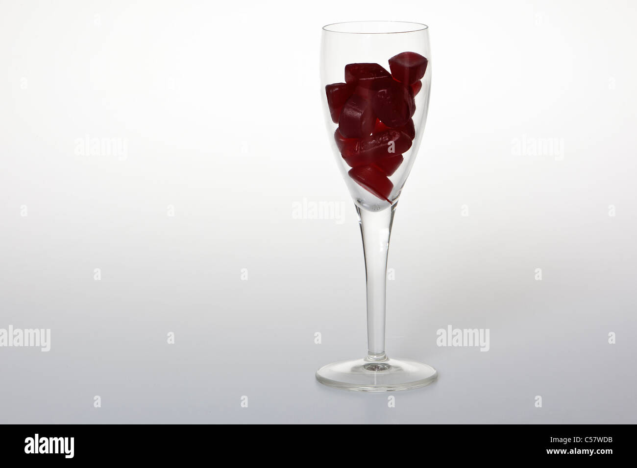 Glas Wein gefüllt mit roten Gummibärchen gegen einen weißen Hintergrund. Stockfoto