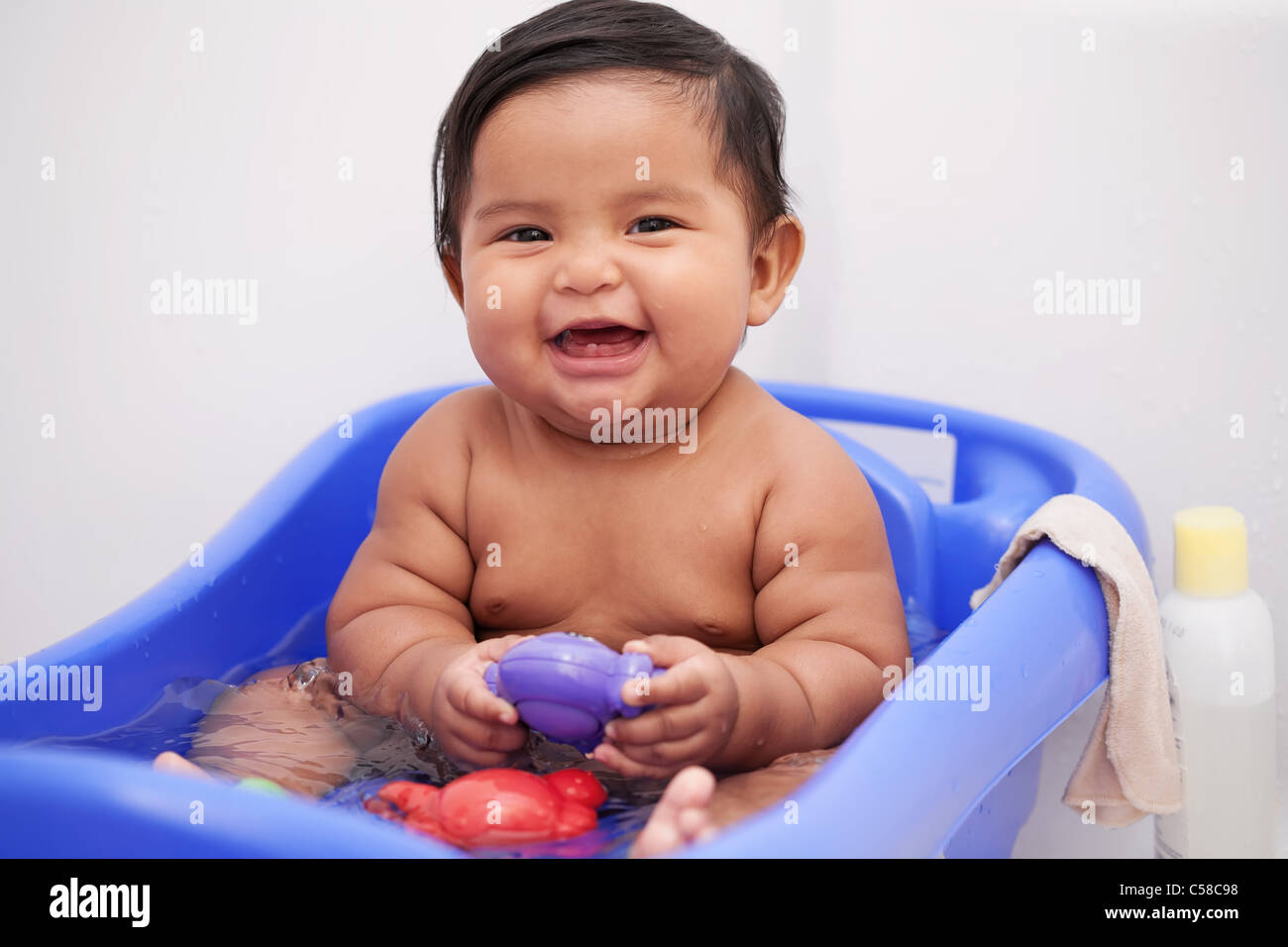 Lächelnd chubby Baby Spielen und Spielzeug in einem mit Wasser gefüllten Baby Badewanne Stockfoto