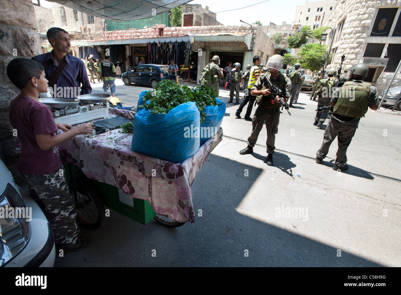 Palästinensische Gemüsestände navigieren schwer bewaffneten israelischen Soldaten in den Straßen von der Westbank-Stadt Hebron. Stockfoto