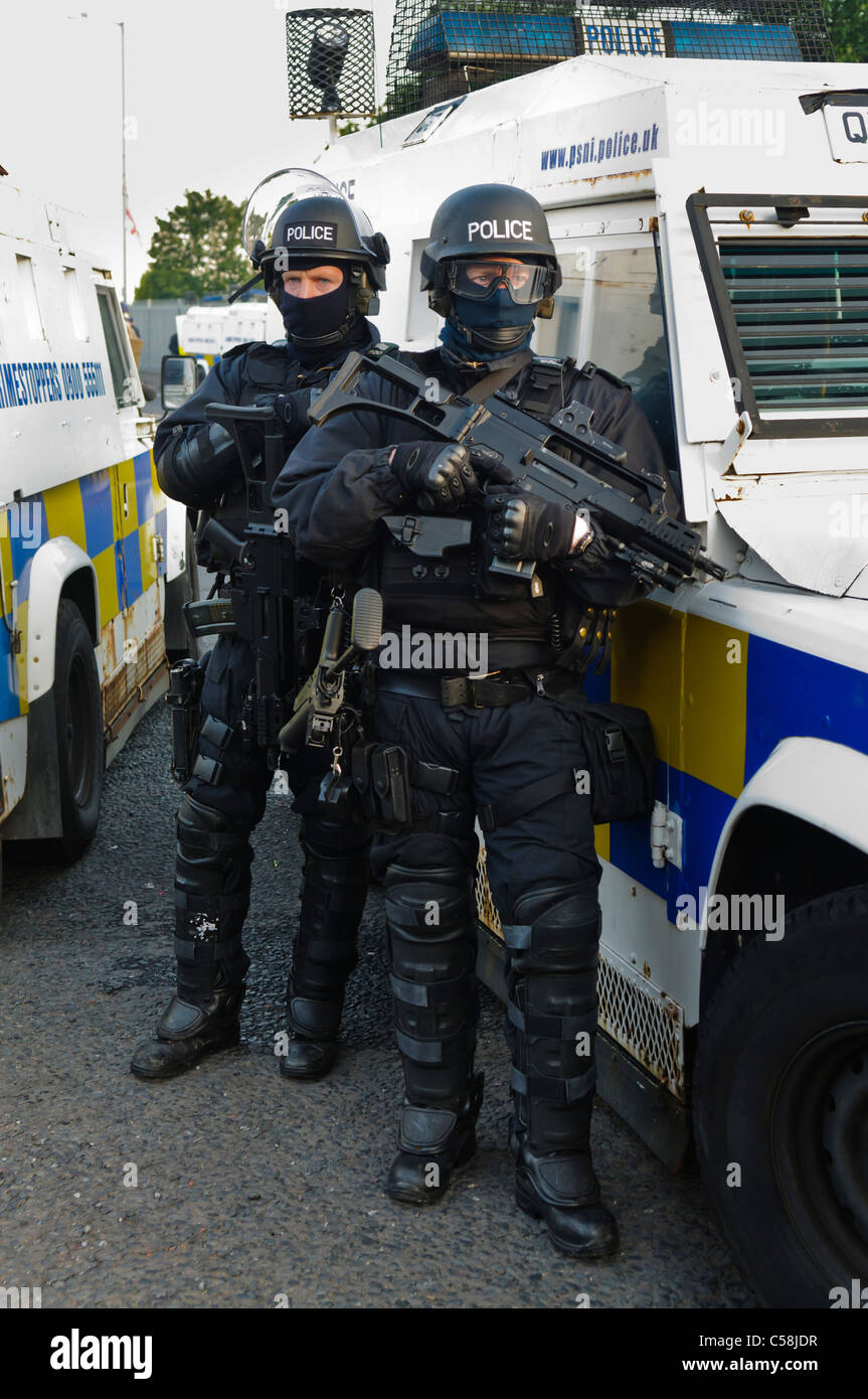 Polizisten in Kampfmontur ein Riot bewaffnet mit einem Heckler & Koch G36C automatische Maschinengewehr Stand neben einem gepanzerten Landrover Stockfoto