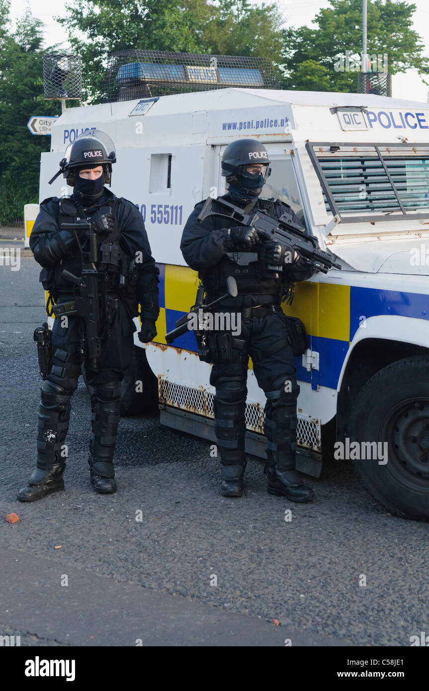 Polizisten in Kampfmontur ein Riot bewaffnet mit einem Heckler & Koch G36C automatische Maschinengewehr Stand neben einem gepanzerten Landrover Stockfoto