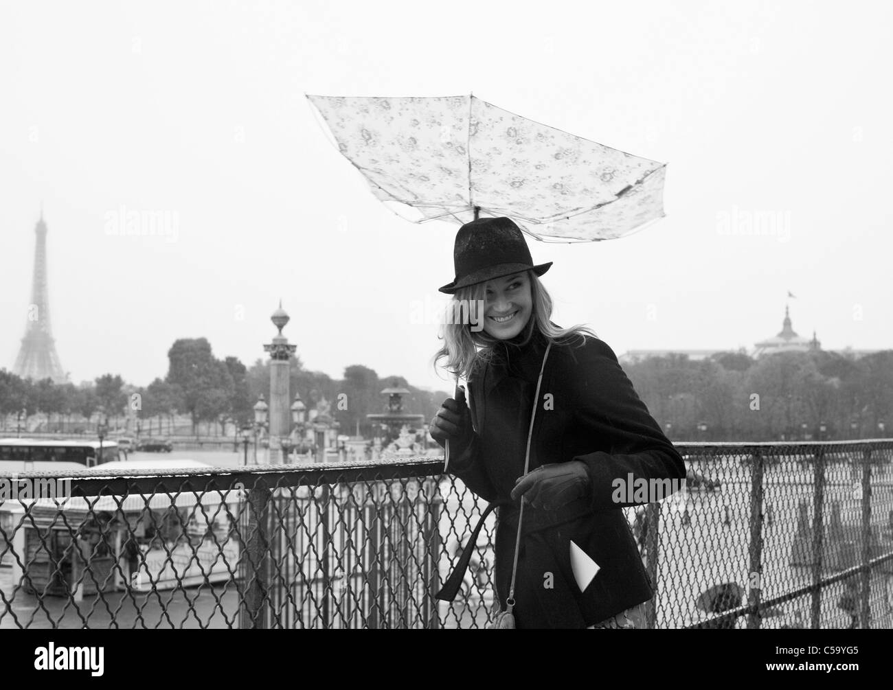 Eine junge Frau lacht wie durch den Wind über den Place De La Concorde ihren Schirm innen nach außen gedreht wird. Paris. Frankreich Stockfoto