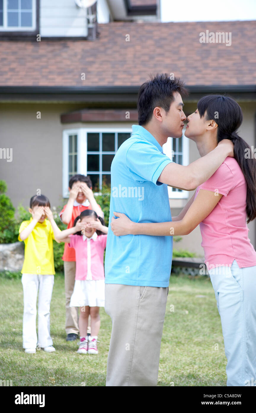 Kinder Hand in Hand auf Augen, während die Eltern küssen im Vordergrund Stockfoto