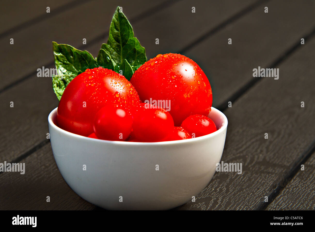 Weiße Schale mit frischen Tomaten und Blätter am schwarzen Tisch Stockfoto