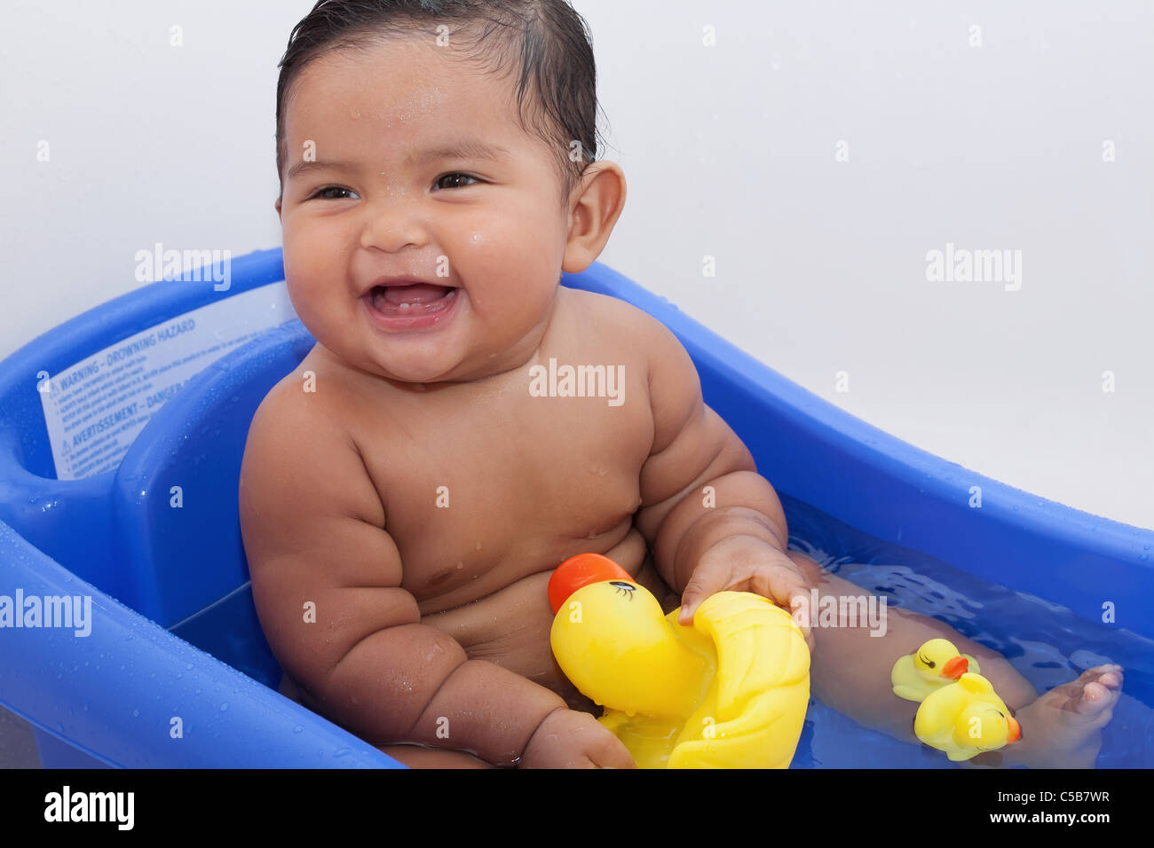 Lachendes Baby spielt mit Gummienten in Badewanne Stockfoto