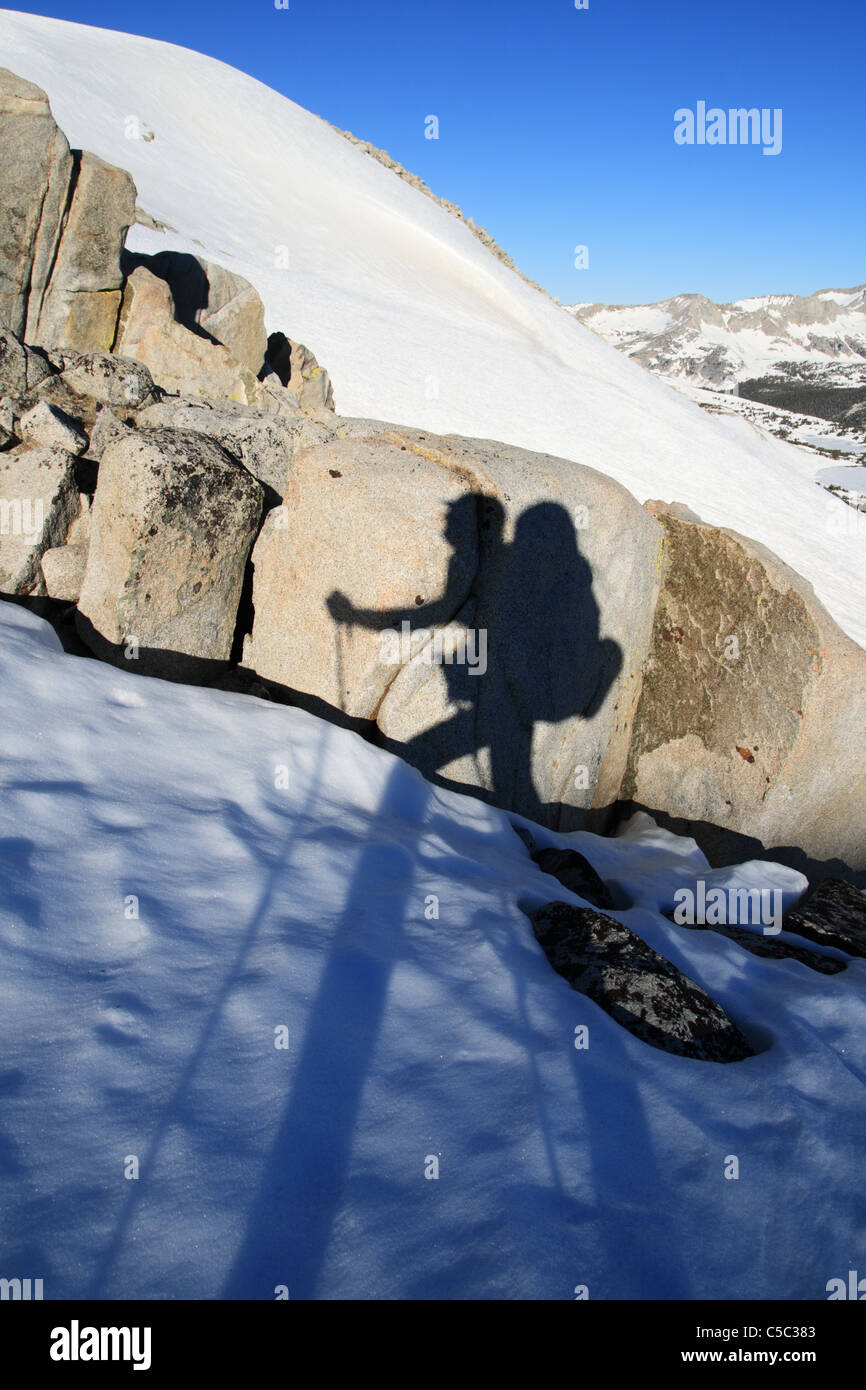 Wanderer mit trekking Stöcke Schatten auf einem Felsen als Wanderer oder Backcountry Skifahrer fährt auf Schnee mit großen Rucksack Stockfoto