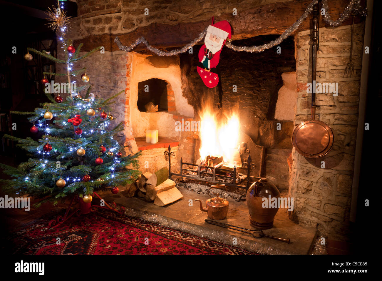 Kaminecke im alten Haus mit hoch lodernden Kaminfeuer und geschmückten Weihnachtsbaum, Bevorratung und Kupfer Wasserkocher. JMH 5161 Stockfoto