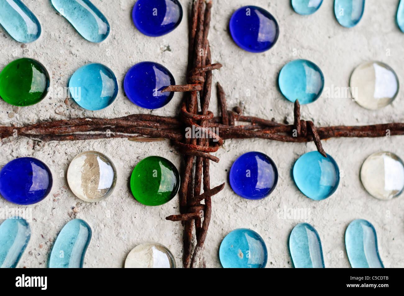 Rostig, Stacheldraht Kreuz auf einem Stein mit farbigem Glas eingebettet Stockfoto