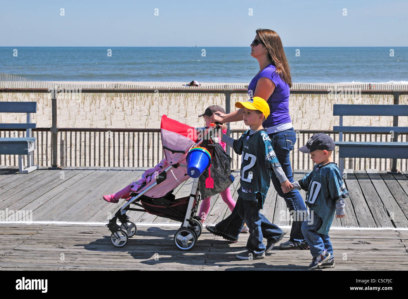 Eine Frau schiebt mit drei kleinen Kindern zu Fuß neben ihr, einen Kinderwagen auf der Promenade in Ocean City, New Jersey Stockfoto