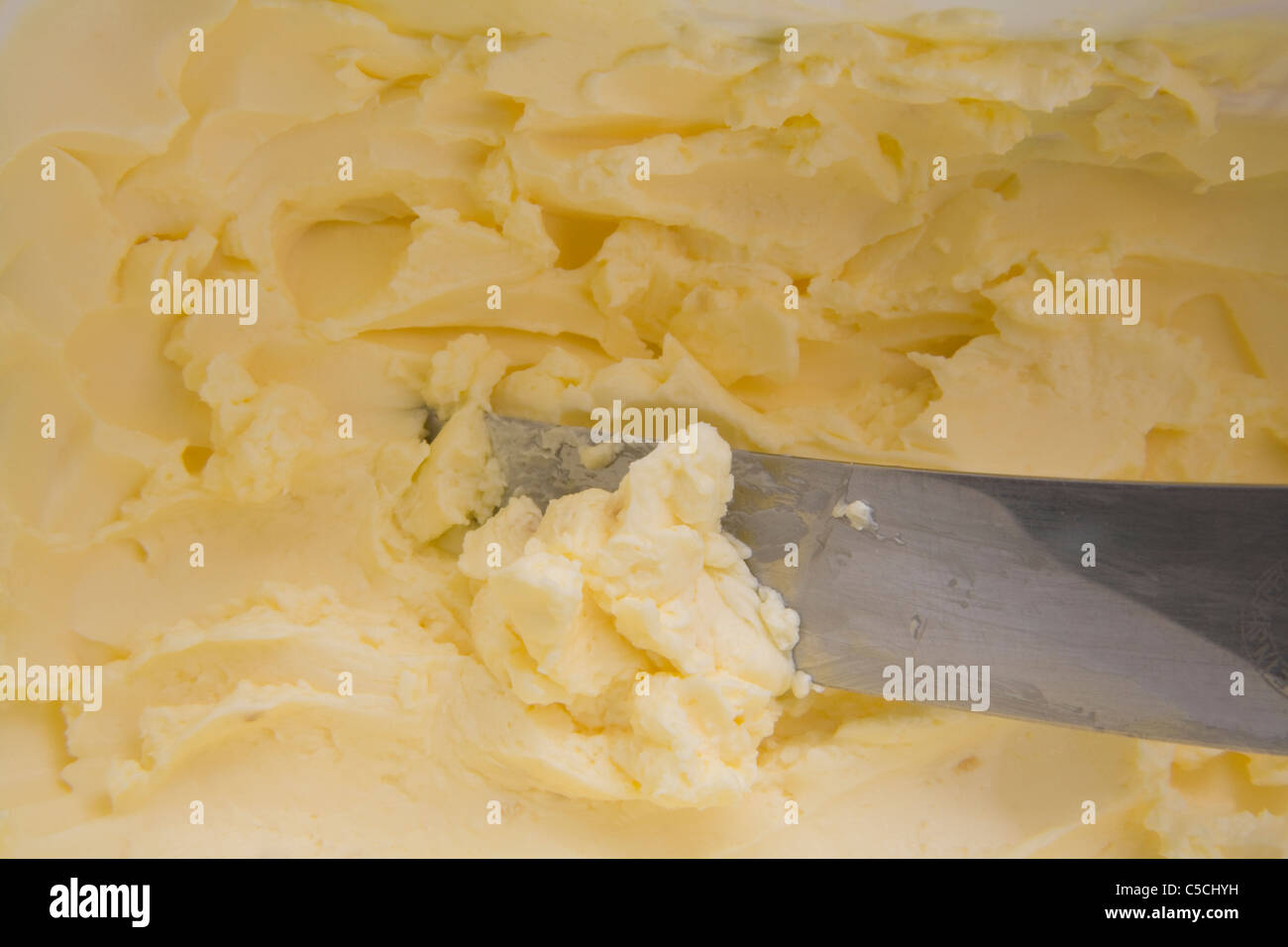 Mit einem Messer einen Knauf fettarmer Margarine aus einer Wanne holen, die 75 % weniger gesättigte Fettsäuren enthält als Butter Stockfoto