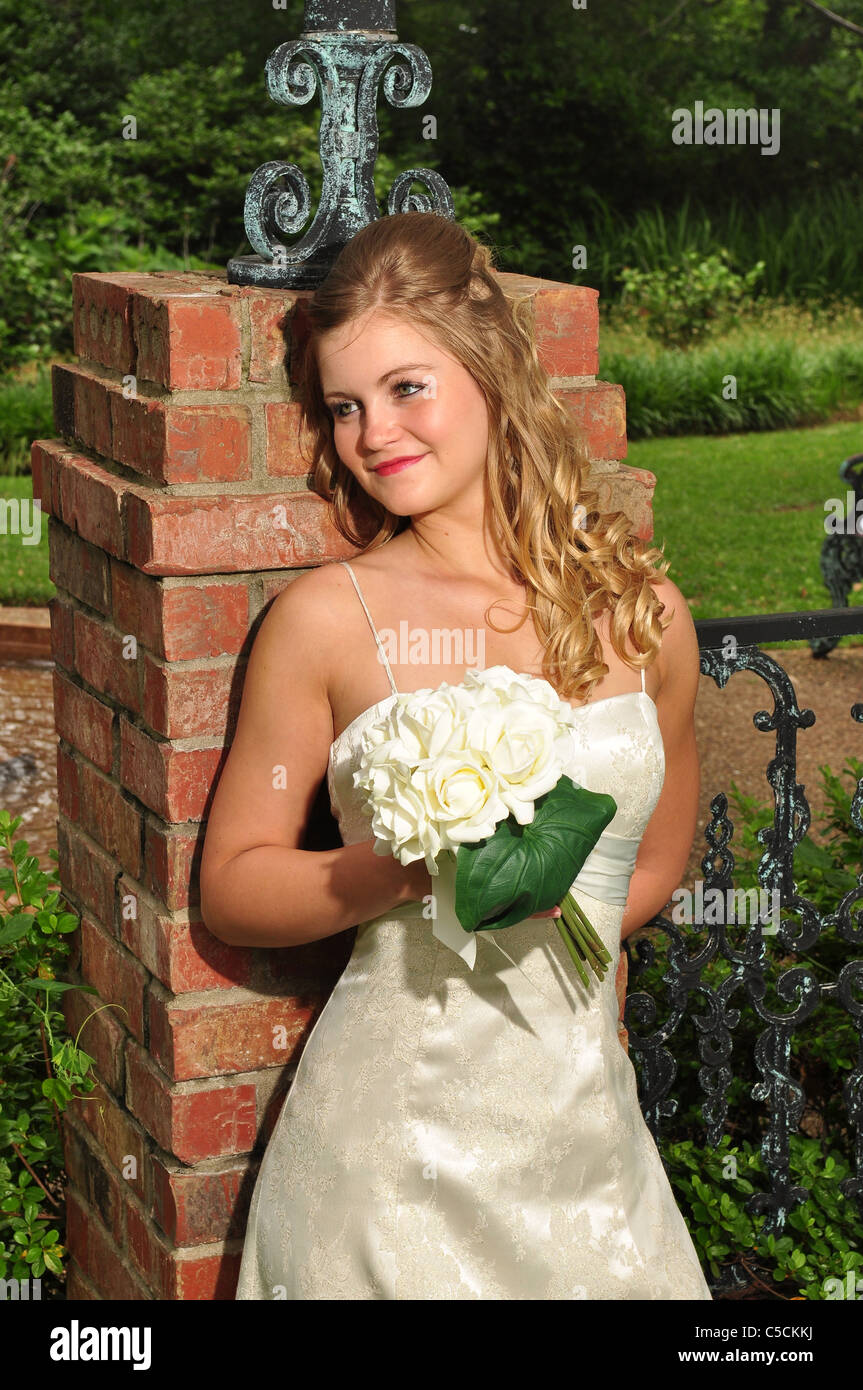 Ein 20 etwas kaukasischen Braut steht außerhalb gegen einen Backstein-Spalte halten ihr Blumen. Stockfoto