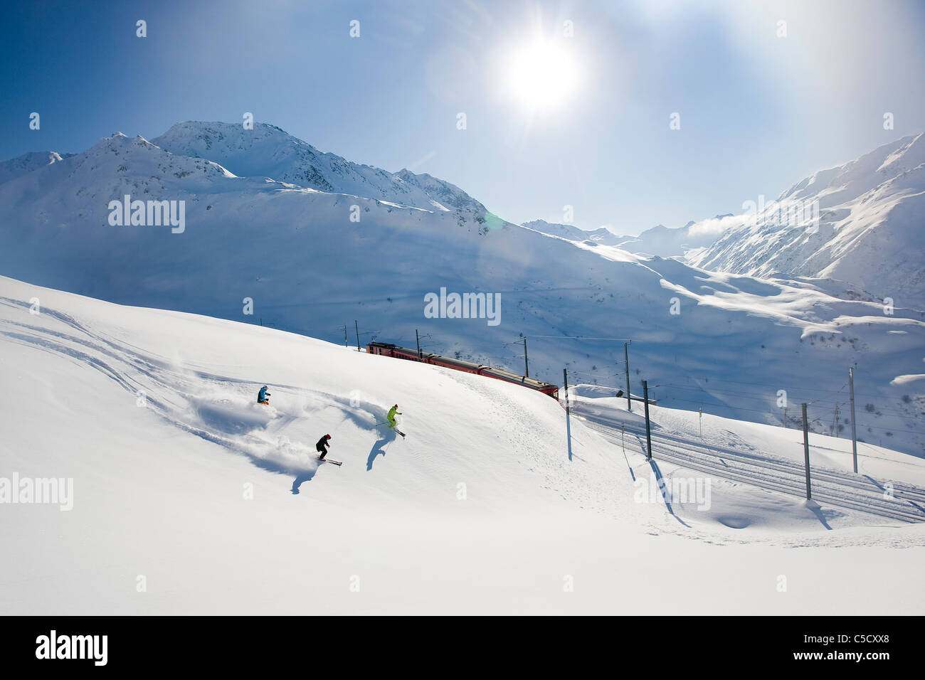 Mittleren Abstand von drei Menschen, die gegen die Alpen und die Sonne Skifahren Stockfoto