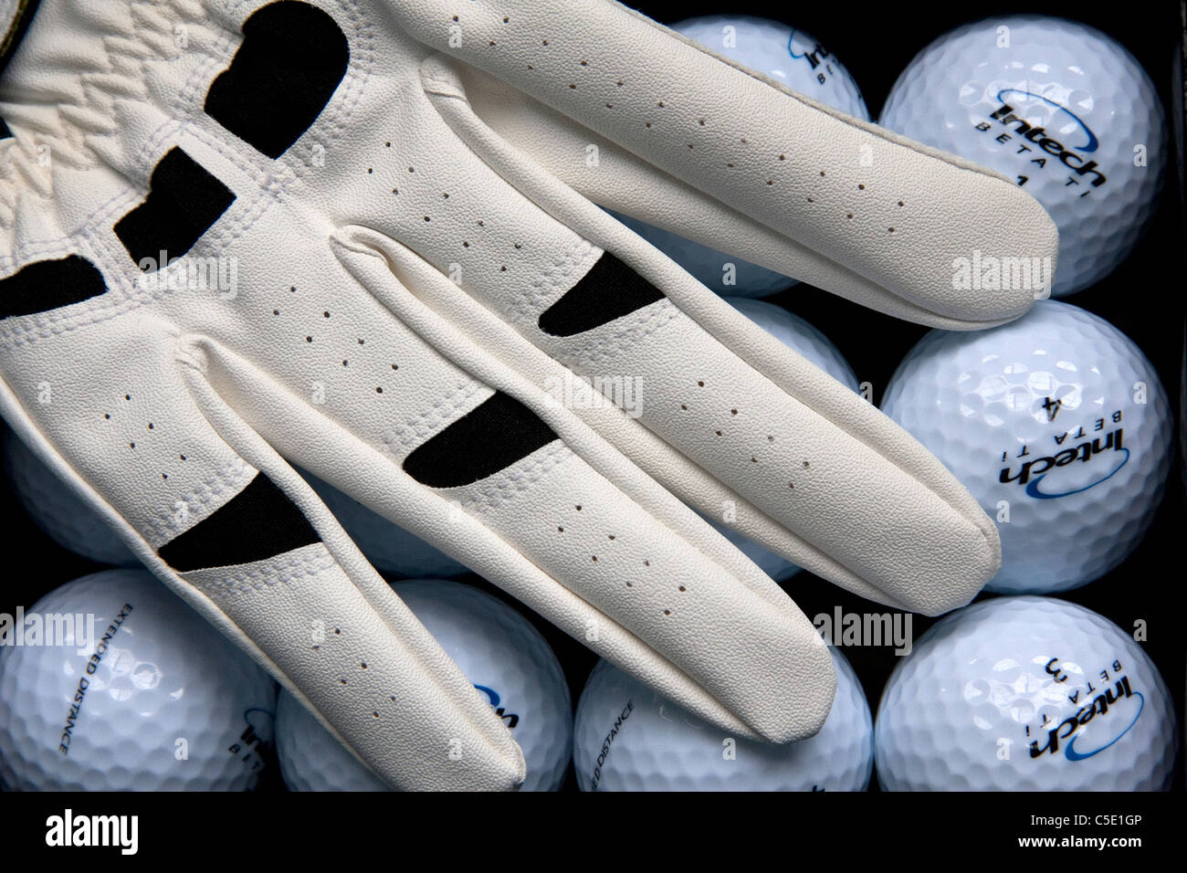 Ein Hintergrund von glänzenden neuen Golfbällen, übersichtlich in Reihen, stellen eine geeignete Kulisse für ein Golfer Handschuh. Stockfoto