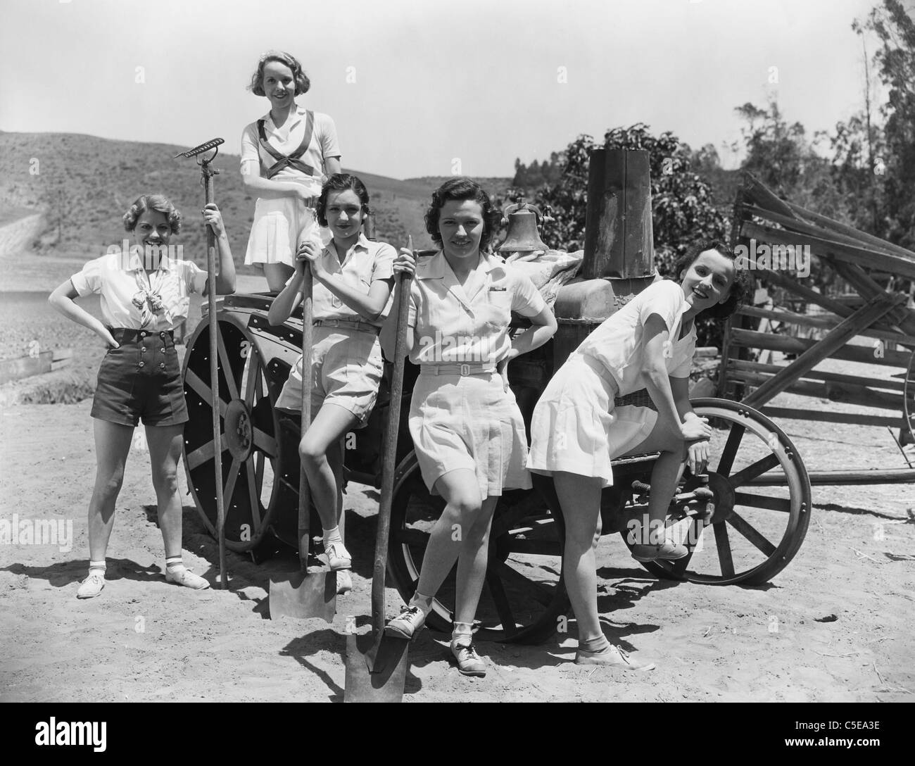 Junge Frauen mit Gartengeräten Stand in der Nähe Holzkarren Stockfoto