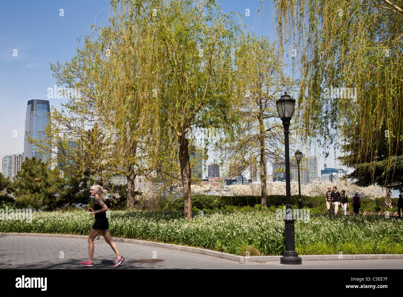 Läufer und Walker, Esplanade in Battery Park City, New Jersey Wolkenkratzern im Hintergrund, NYC Stockfoto