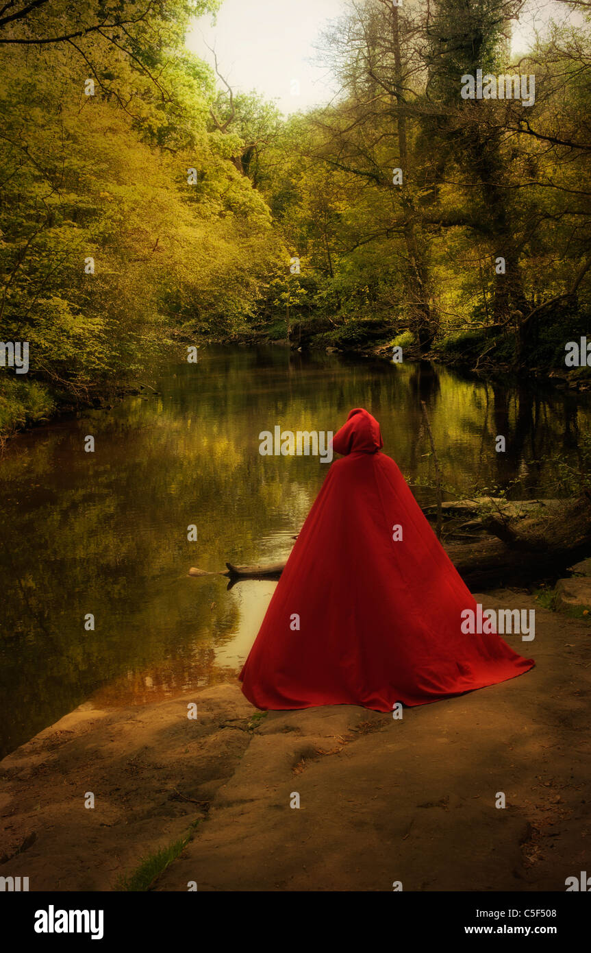 Geheimnisvolle Person im roten Umhang im Wald am See Stockfoto