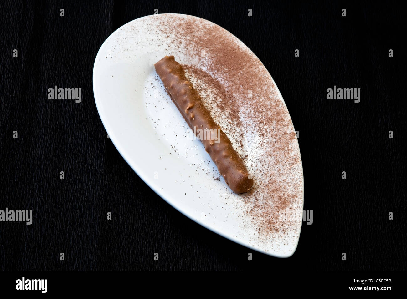 eine lange Schokolade Praline auf einem weißen Teller mit Kakaopulver Stockfoto
