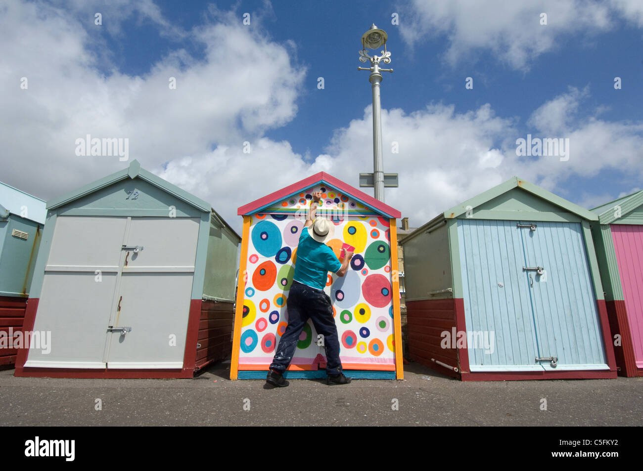 Eine Mitte im Alter Mann trotzt er Regeln und Malerei seine Brighton Strandhütte in Nichtregelung bunte Flecken. Stockfoto