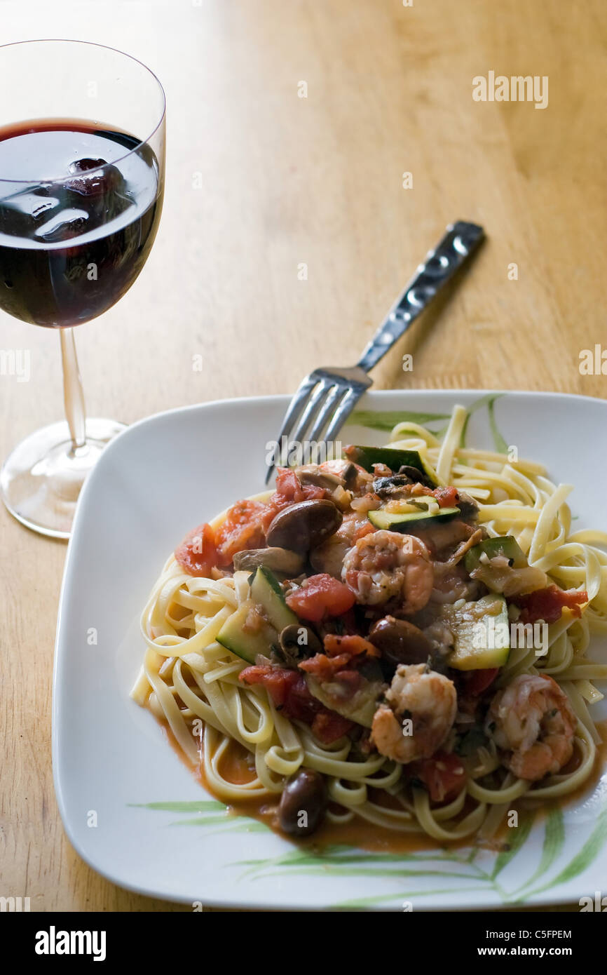 Eine leckere Garnelen und Pasta Gericht zusammen mit einem Glas Rotwein. Stockfoto
