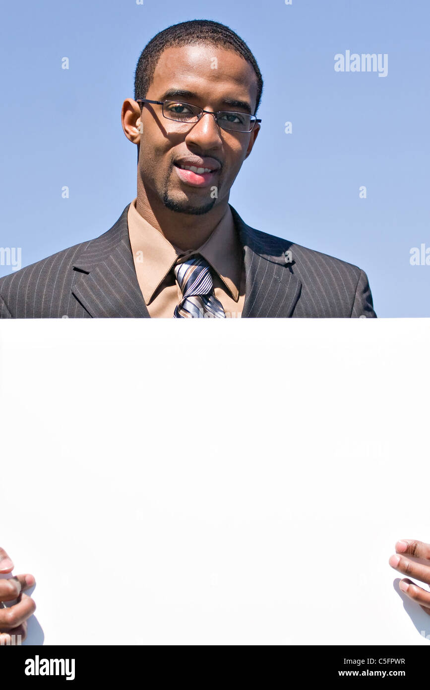 Ein junger Mann hält ein leeres weißes Schild mit Exemplar. Stockfoto
