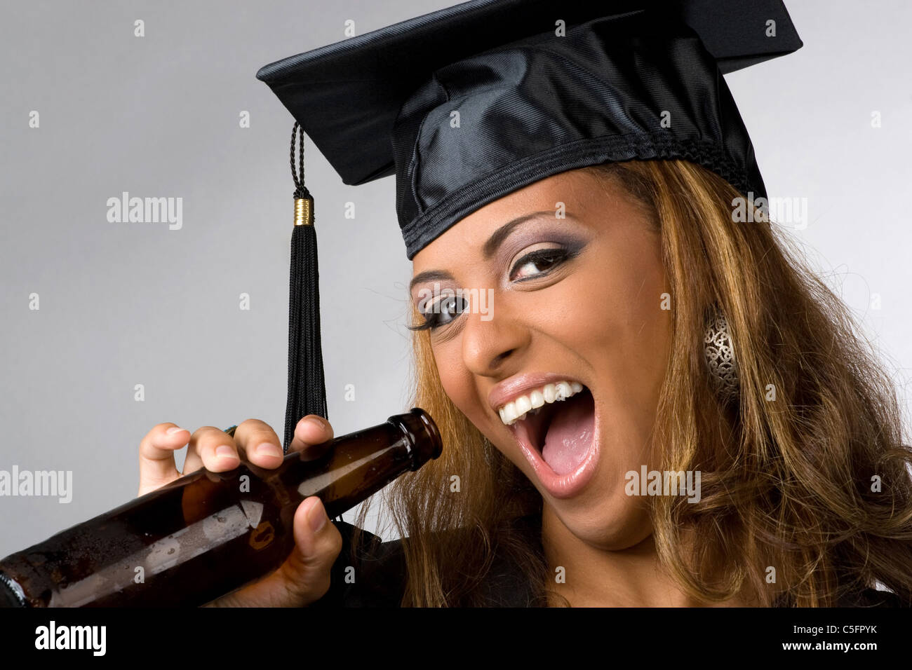 Hochschulabsolvent posiert in ihrer Mütze und Mantel Bierflasche über silbernem Hintergrund isoliert halten. Stockfoto