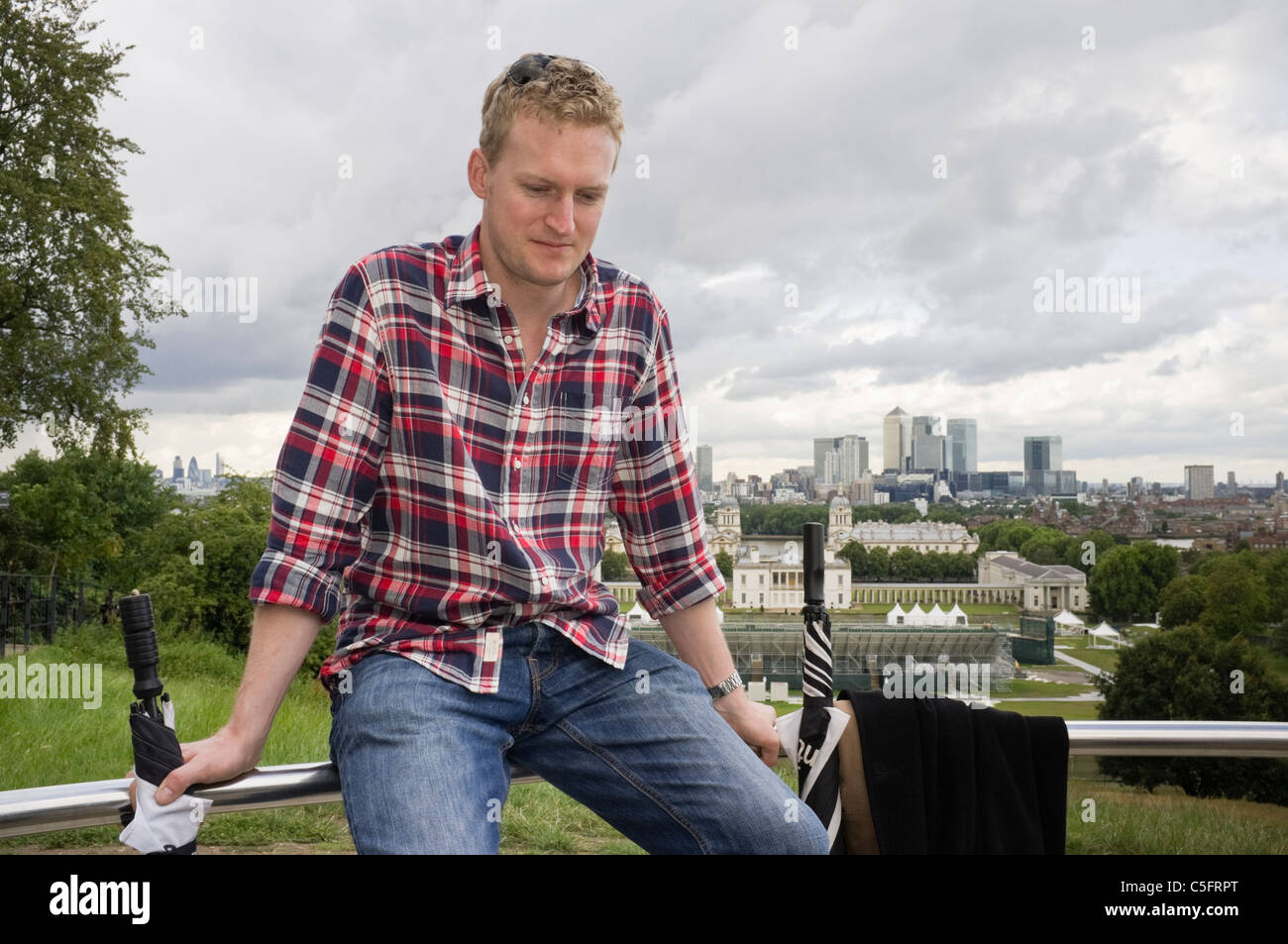 Foto eines modernen, tausendjährigen Mannes, der auf dem Zaun sitzt, der mit Blick von der Sternwarte aus nachdenklich aussieht. Greenwich London England Großbritannien Stockfoto