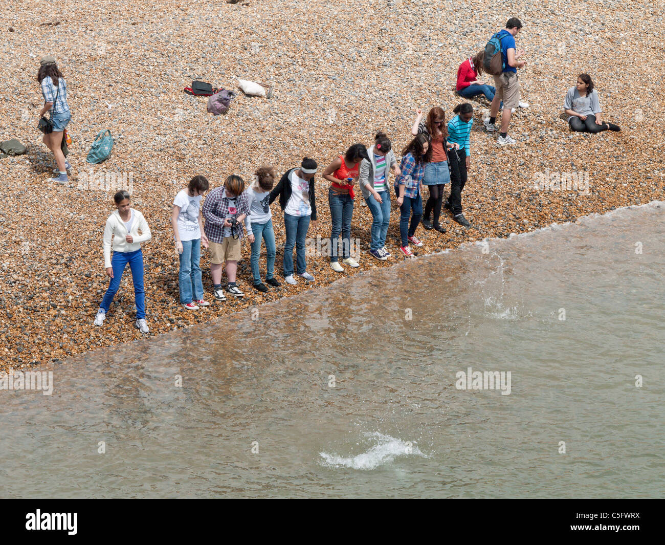eine Reihe von ausländischen Studierenden trotzen der Waveson am Strand in Brighton, Sussex, England Stockfoto