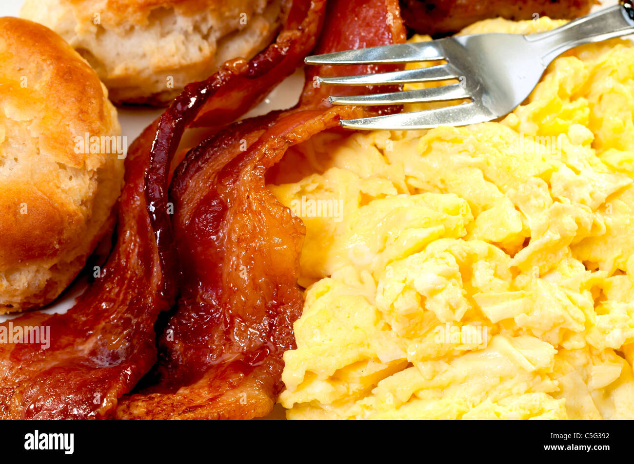 Nahaufnahme von Rührei, Speckscheiben, Kekse und Gabel Stockfoto