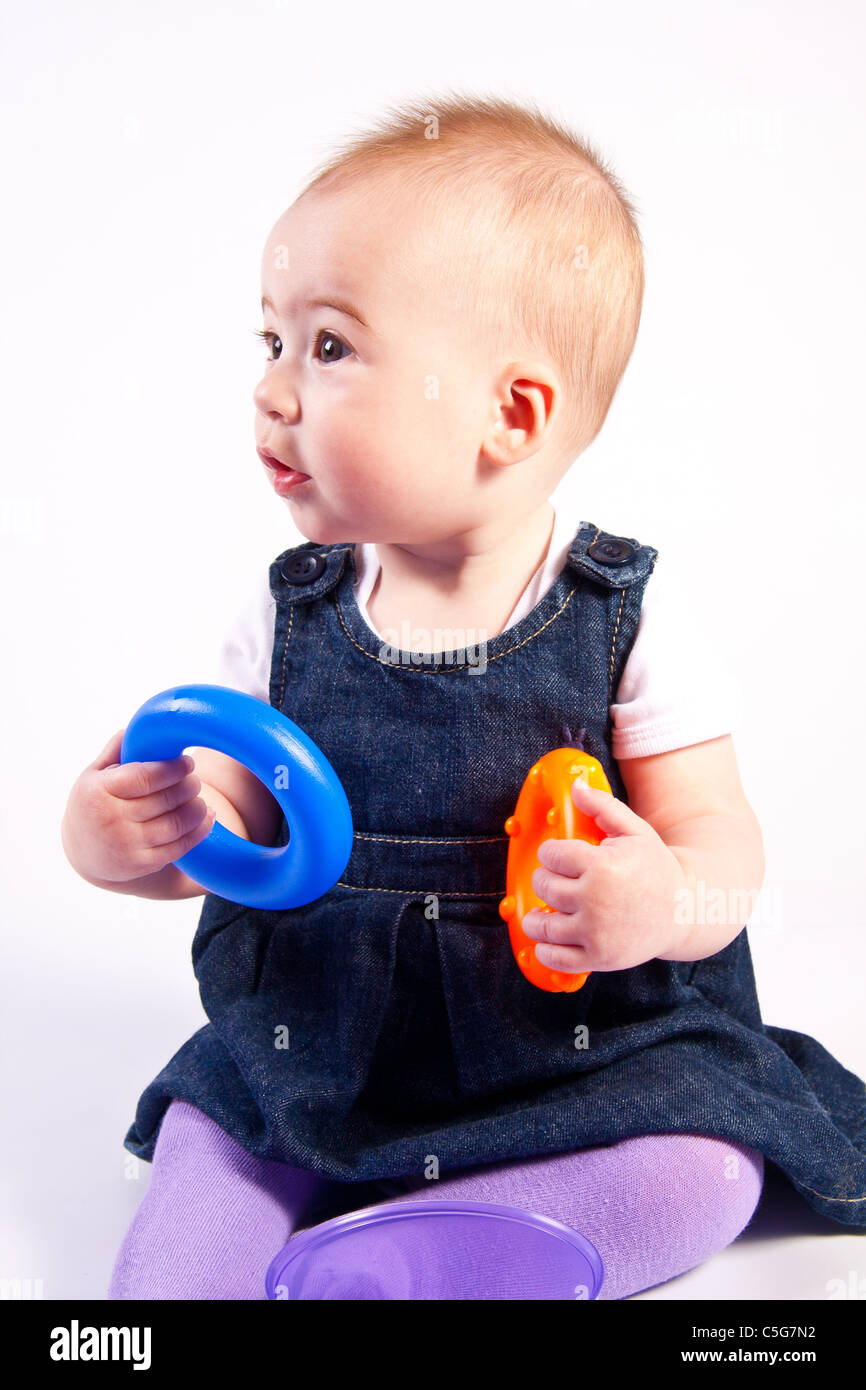 6 Monate altes Baby Mädchen spielen mit farbigen Spielzeug isoliert auf weiss Stockfoto