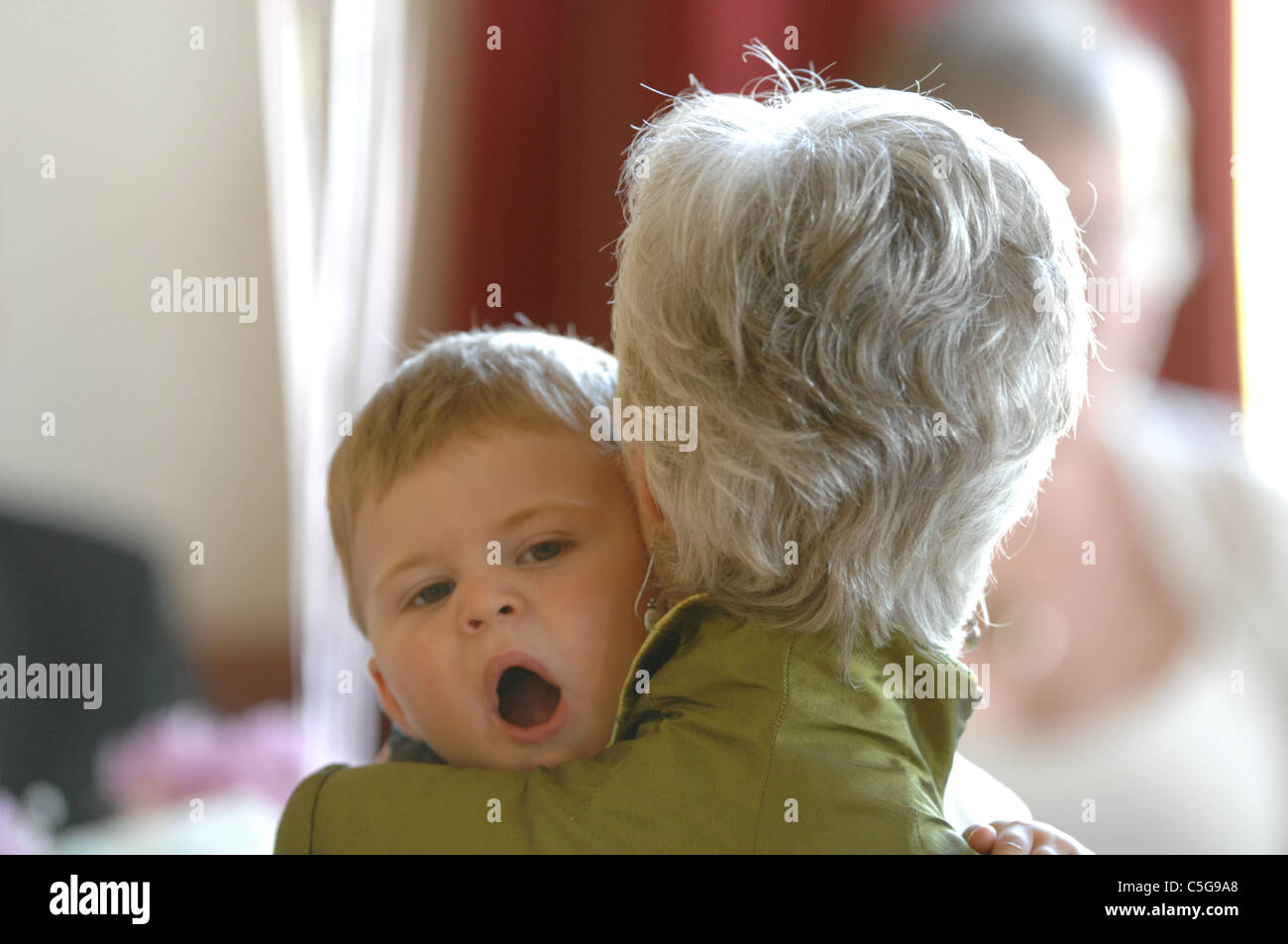 Ein Gähnen Kleinkind, getragen von einer Frau UK Stockfoto