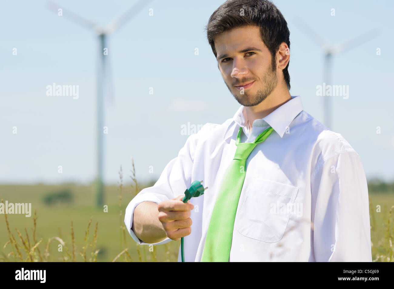 Grüne Energie - Jungunternehmer halten Stecker im Feld mit Windmühle Stockfoto