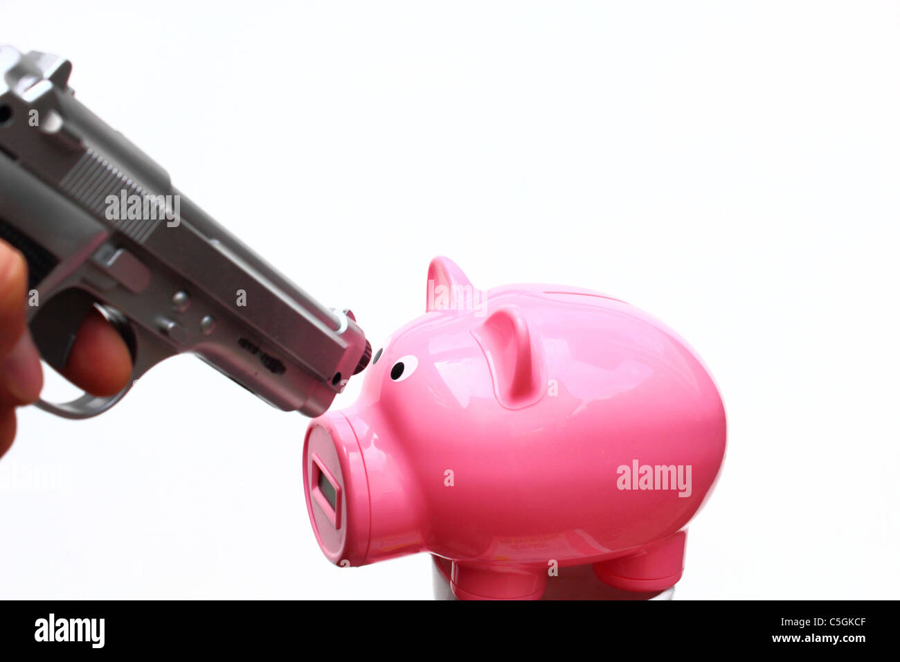 Eine silberne Pistole ist auf ein rosa Sparschwein gerichtet. Stockfoto