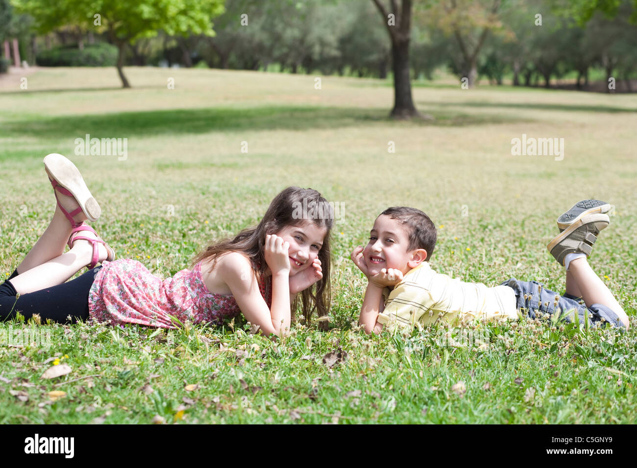 Niedlichen Kinder legen sich auf grünem Rasen und suchen einander im Park, im freien Stockfoto