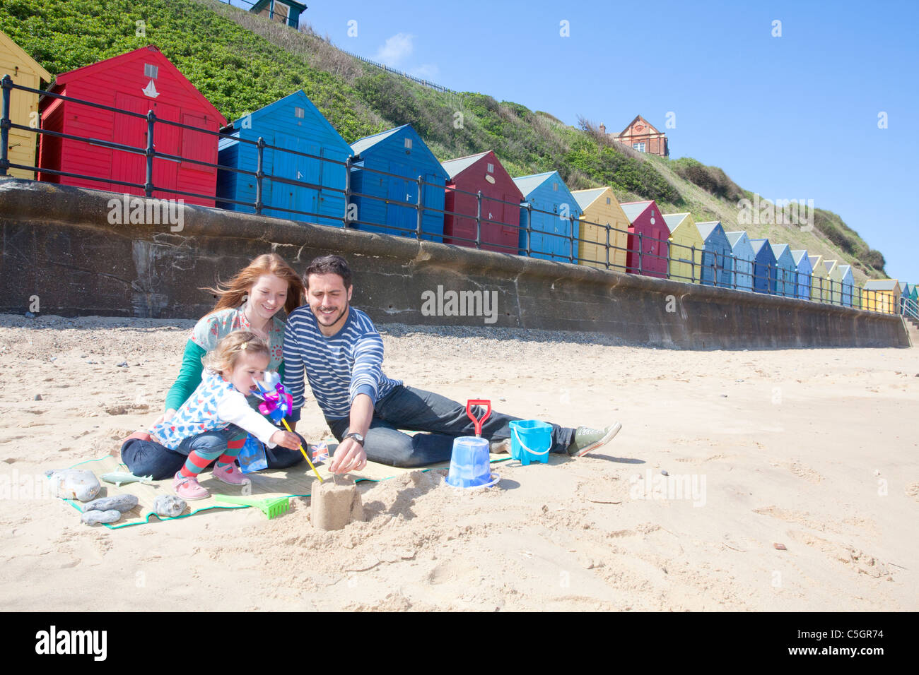 Junge Familie Sandburgen am Strand vor Strandhütten am Mundesley an der Küste von Norfolk Stockfoto