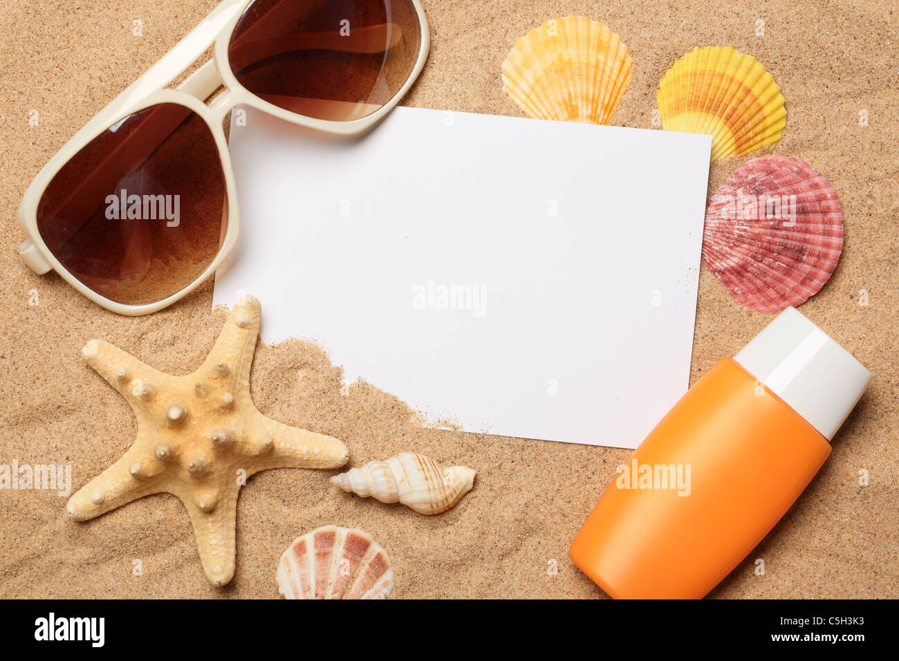 Sonnenbrille, Sonnencreme und Muscheln mit einer leeren Karte auf Sand. Stockfoto