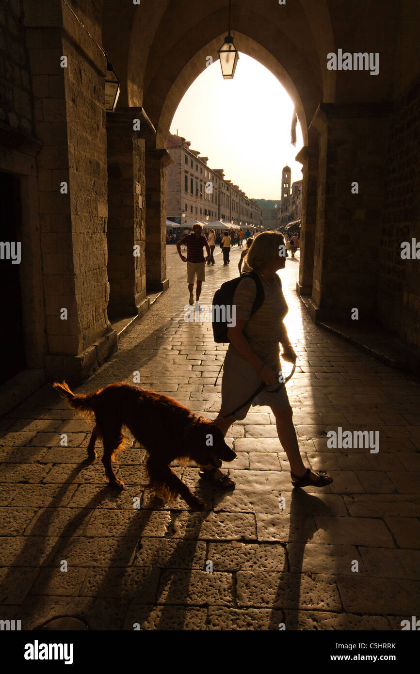 Frau mit Hund am Eingang zur Altstadt, Silhouette gegen den goldenen Nachmittagssonne zu Fuß. Stockfoto