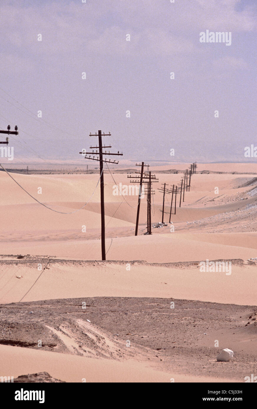 Elektrische und Telefonleitungen marschieren in einer Linie durch die Sahara-Wüste in Ägypten. Stockfoto
