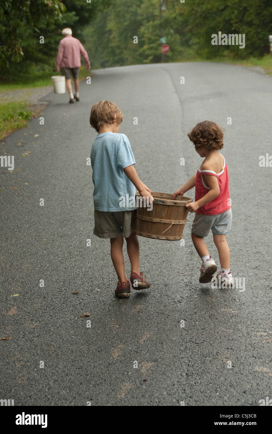 zwei Kinder und Adault zu Fuß unterwegs mit Schaufel und Korb Stockfoto