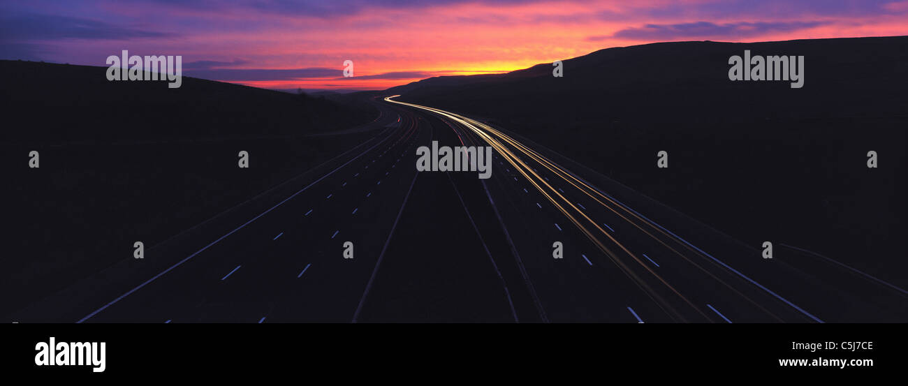 Lebendige Sonnenuntergang Himmel über dunklen Autobahn mit Streifen Lichter von Fahrzeugen, M4 Autobahn, Cumbria, England, UK Stockfoto