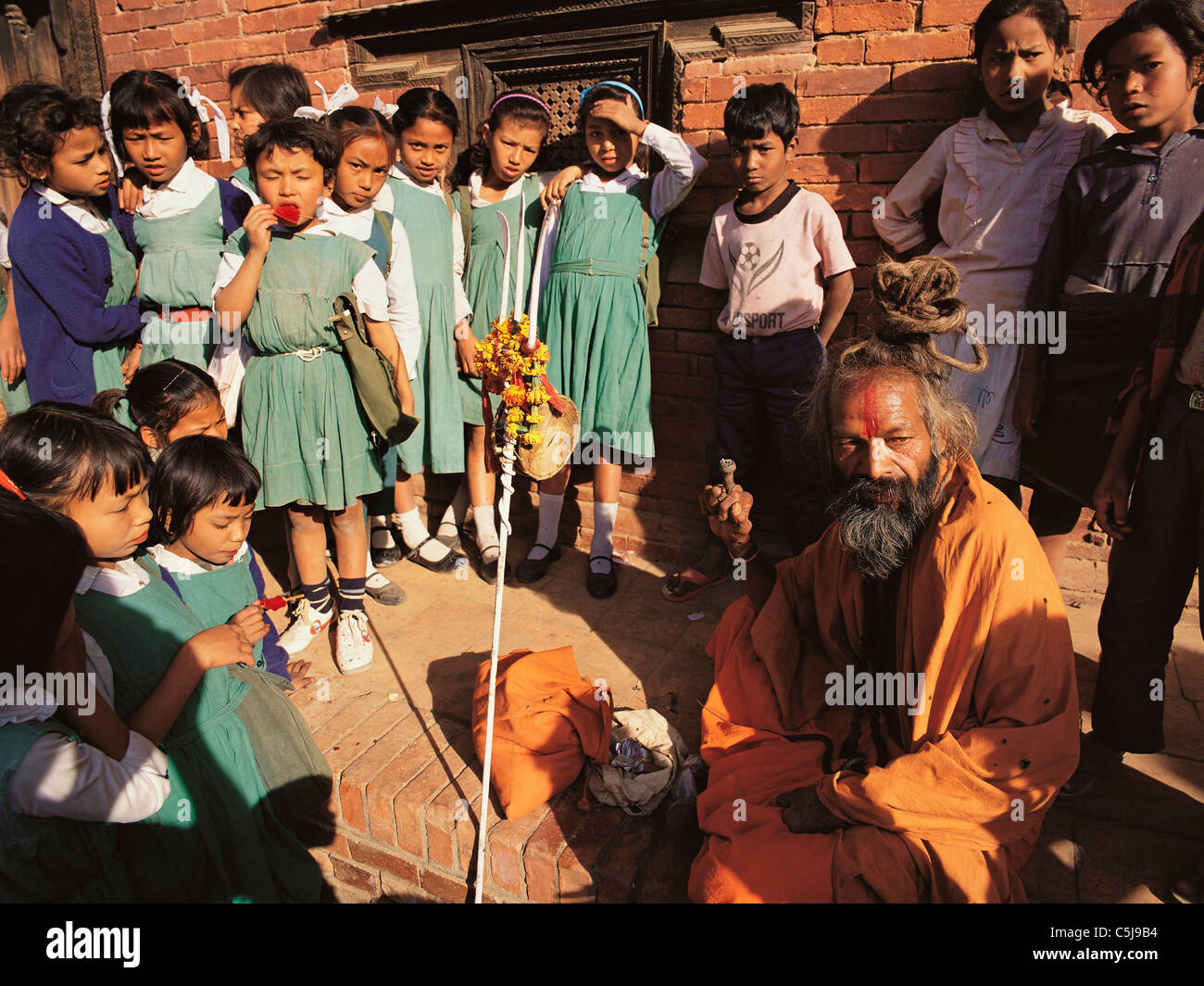 Eine Gruppe von jungen SchülerInnen sammelt Runde fasziniert von einer hinduistischen heiligen Mann oder Saddhu außerhalb der ehemaligen Königspalast in Patan in Stockfoto
