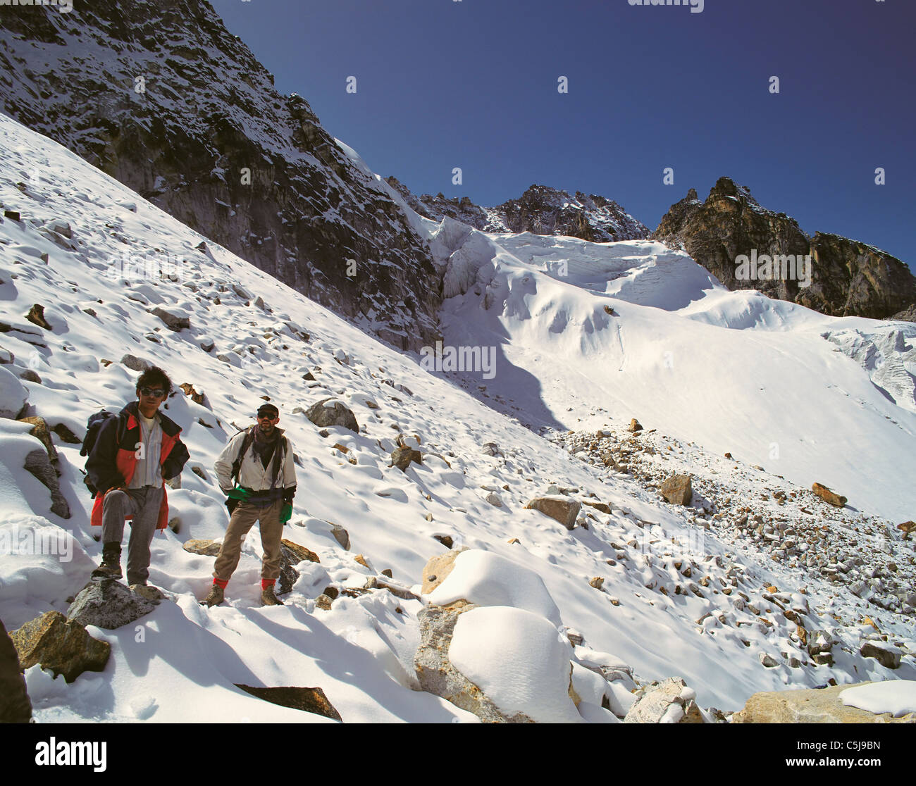 Trekker Rest im oberen Bereich der 18000 Fuß Lapsang-La Pass mit Gletschern und Felsspitzen hinter Kangchenjunga und Umgebung Stockfoto
