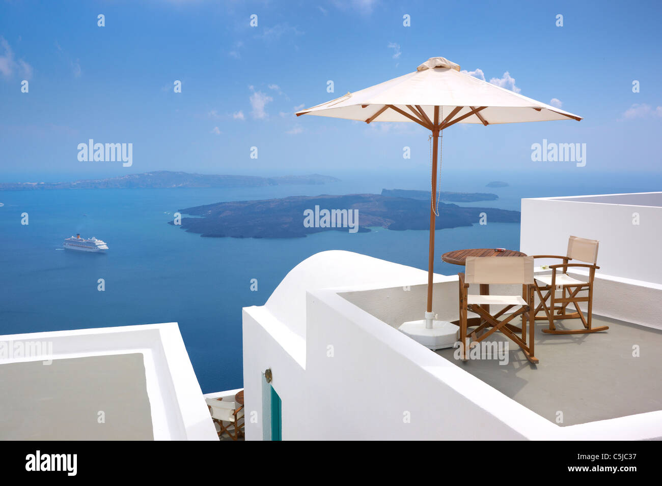 Thira (Hauptstadt von Santorini) - Terrasse mit Liegestühlen, Sonnenschirm und blauen Meer im Hintergrund, Insel Santorin, Griechenland Stockfoto