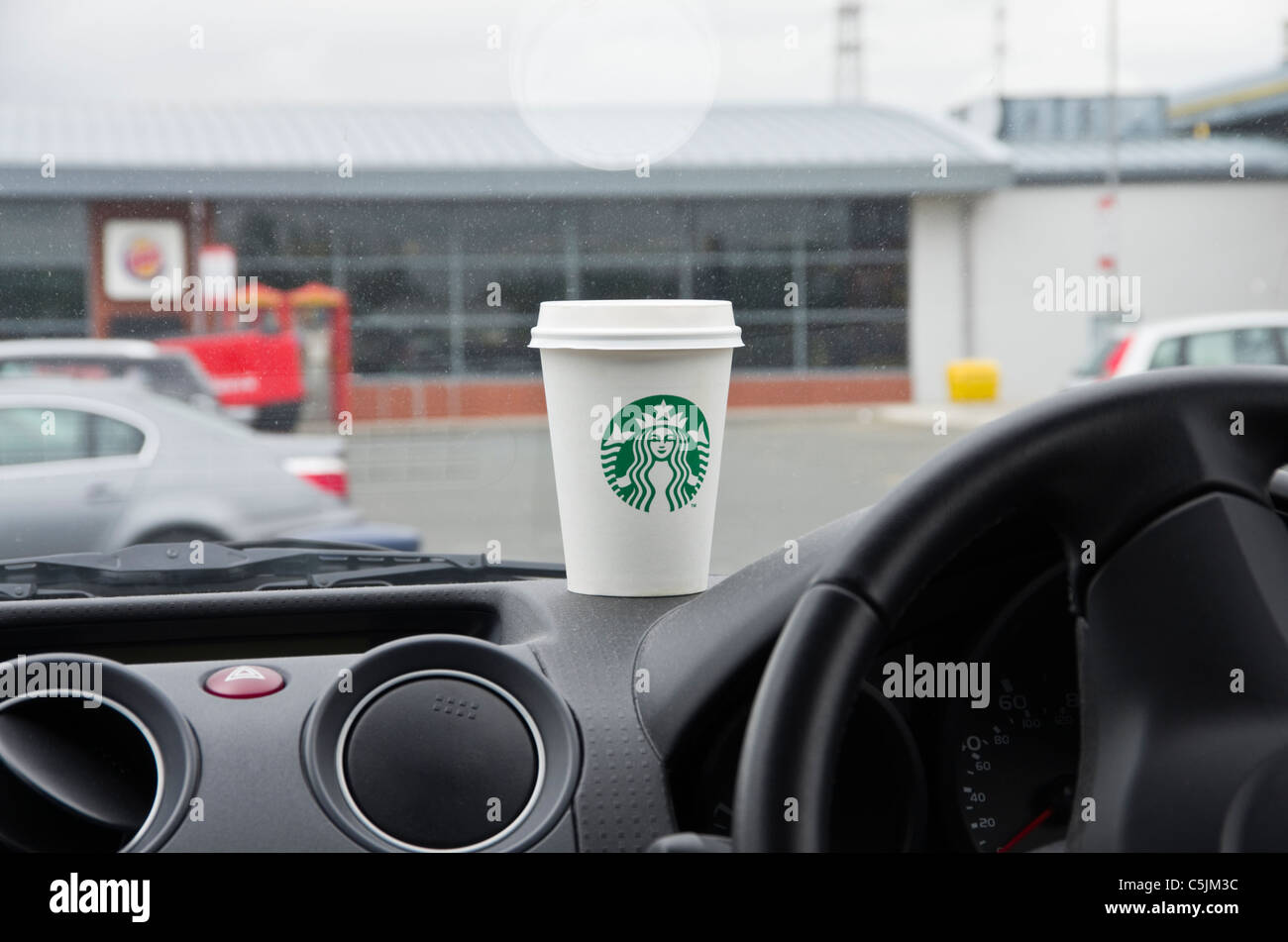 Starbucks-Kaffee in einem Pappbecher zum mitnehmen auf dem Armaturenbrett eines Autos in einer Autobahn-Tankstelle gehen. England, UK Stockfoto
