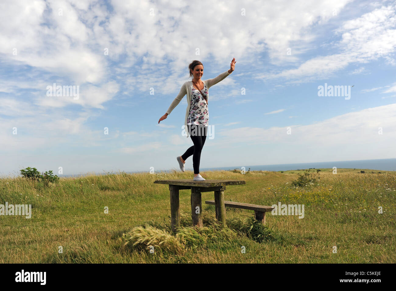 Junge Frau, die Spaß springen auf einem Picknick-Tisch auf tiefen Sheepcote Tal in der Nähe von Brighton, Sussex UK Stockfoto