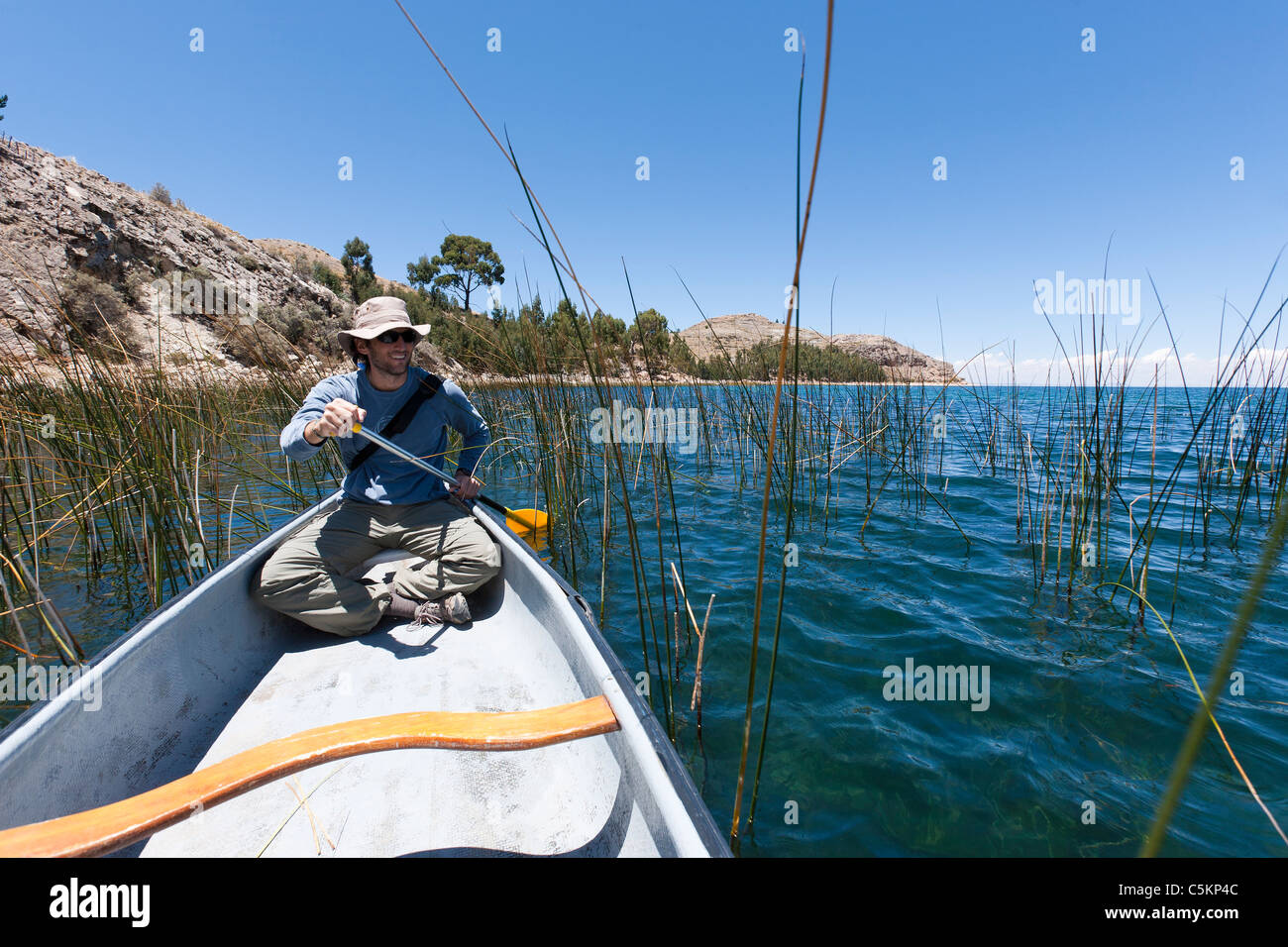 Ein Mann paddelt ein kanadisches Kanu auf dem Titicacasee von Schilfhäusern, der einzige private Insel auf dem Titicacasee. Stockfoto