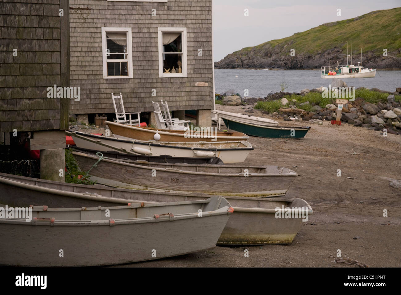 Monhegan Island, Maine - Dories aufgereiht auf Fish Beach neben grauen geschuppter Hütte. Im Hintergrund ist ein Fischerboot in Stockfoto