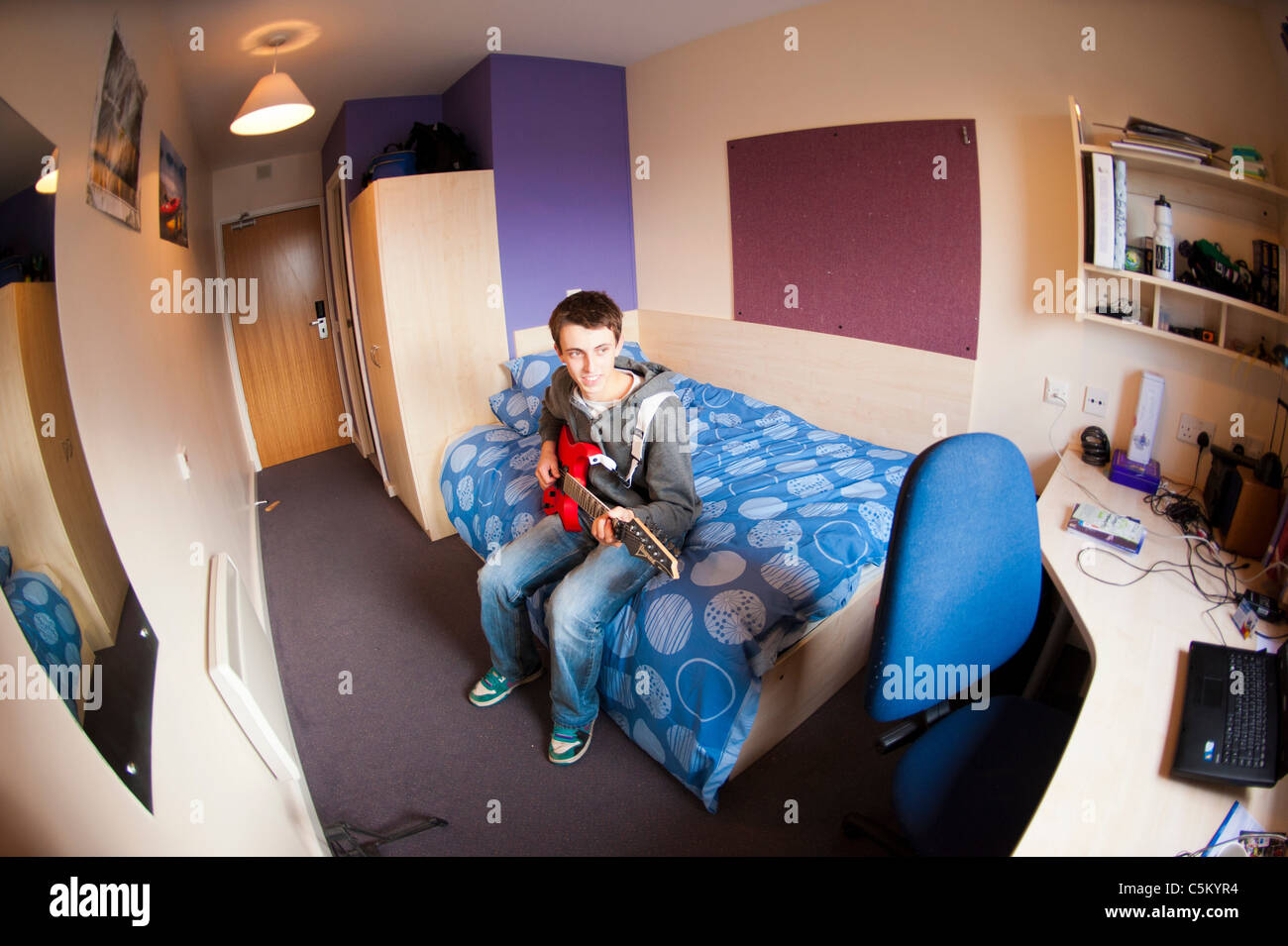 Junger kaukasischer Student, der in seinem Zimmer in den Studentenwohnheimen auf seinem Bett sitzt und eine rote Gitarre spielt. Stockfoto Junger kaukasischer Student, der in seinem Zimmer in den Studentenwohnheimen auf seinem Bett sitzt und eine rote Gitarre spielt. Stockfoto