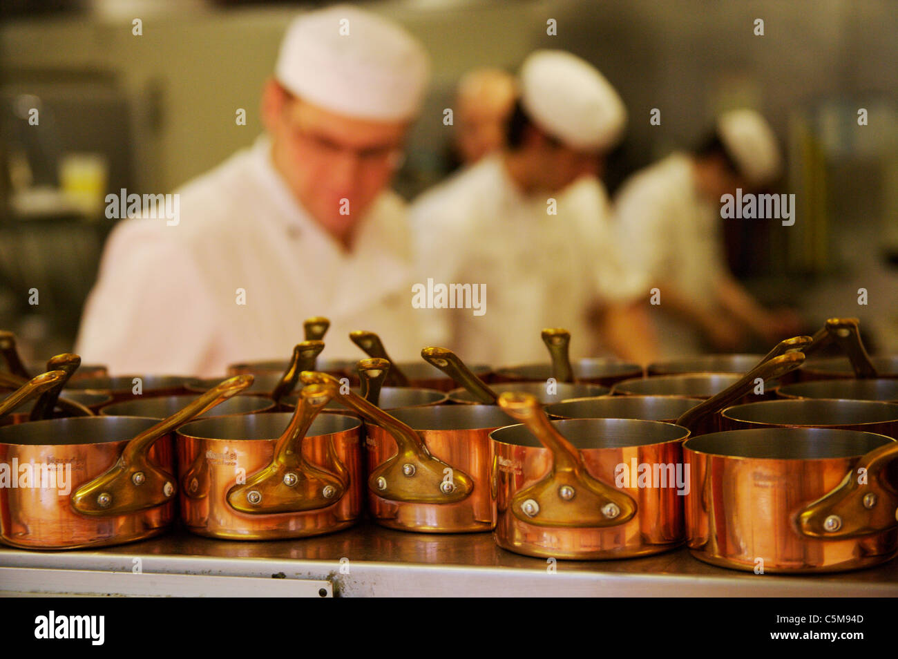 Kupfer Pfannen im Fokus auf einem Regal im Vordergrund mit Köchen, Unscharf im Hintergrund in ein geschäftiges Hotel Küche arbeiten. Stockfoto