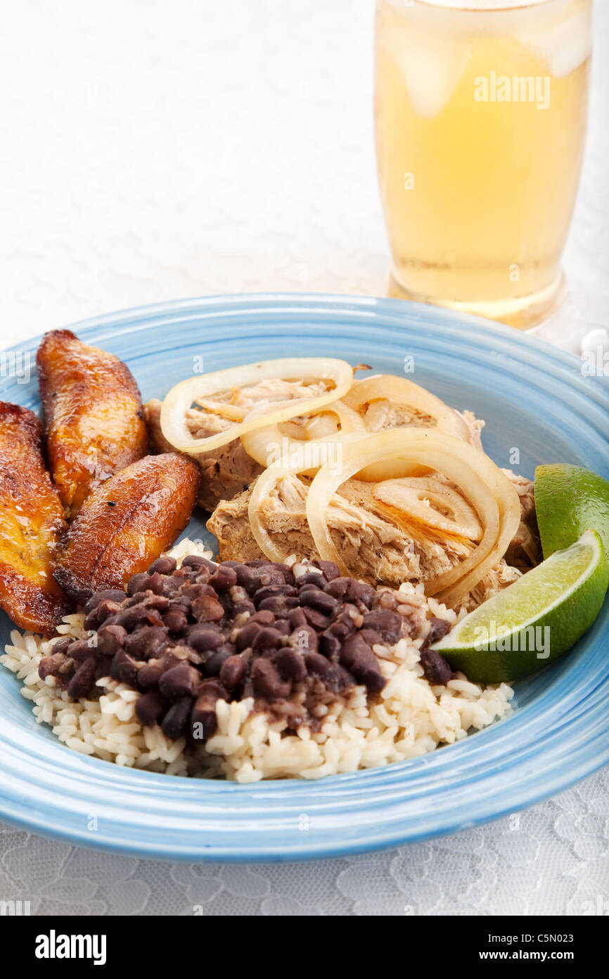 Traditionelle kubanische Abendessen aus schwarzen Bohnen und Reis, Schweinebraten und gebratene Bananen mit einem Glas Eistee. Stockfoto